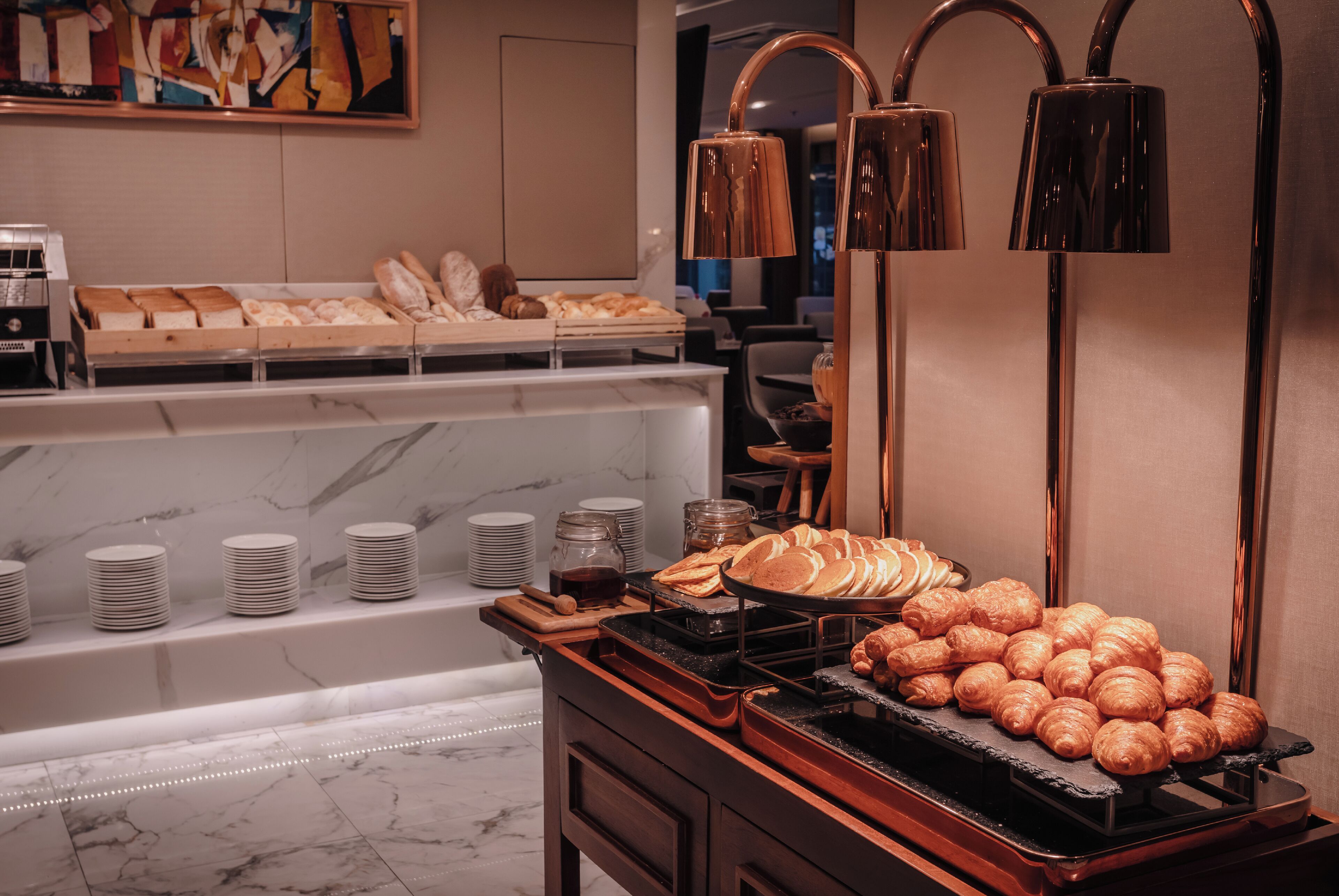 A breakfast buffet with pastries, bread, and a coffee station.