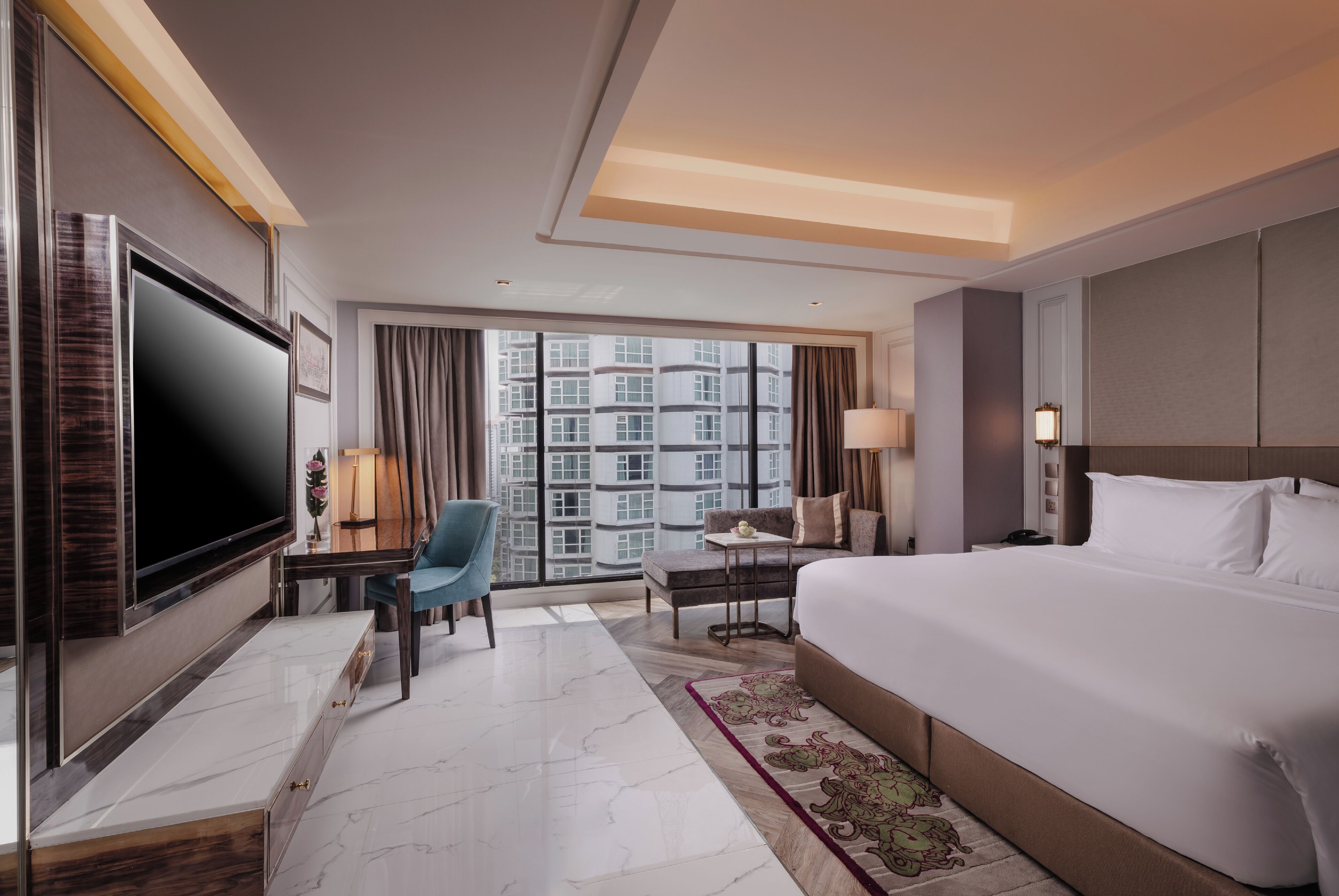 A hotel room with a large bed, a flat-screen TV, a desk with a chair, a sofa, and a large window with a city view.