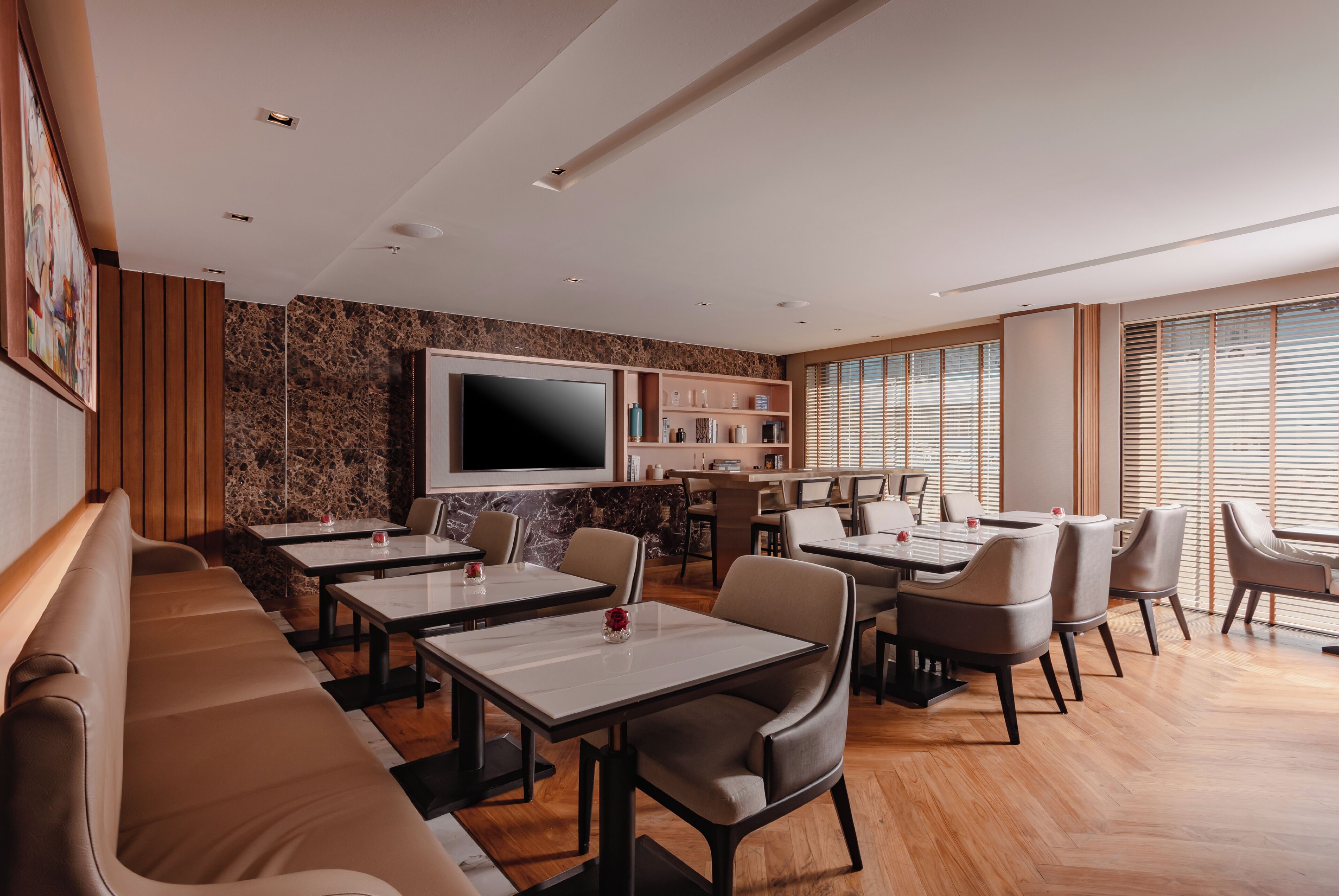 A modern restaurant with a long counter, multiple tables, and a large TV screen.
