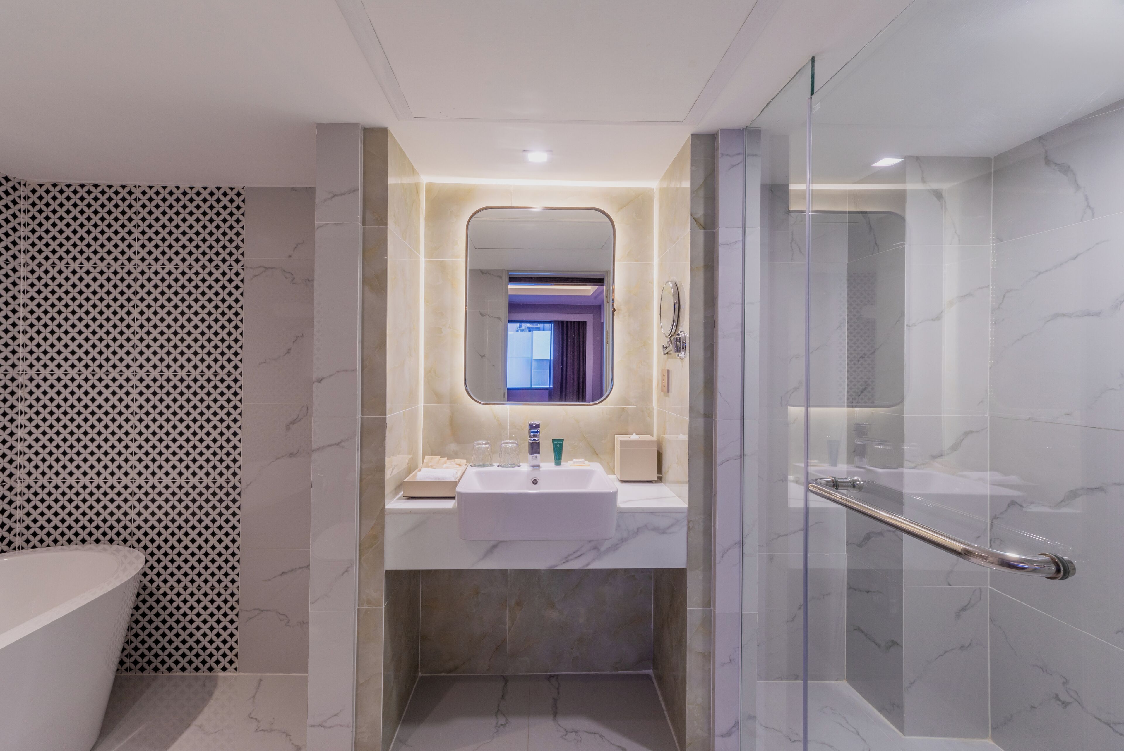 Une salle de bain moderne avec une douche à parois de verre, un lavabo doté d’articles de toilette et un mur décoré d’un motif.