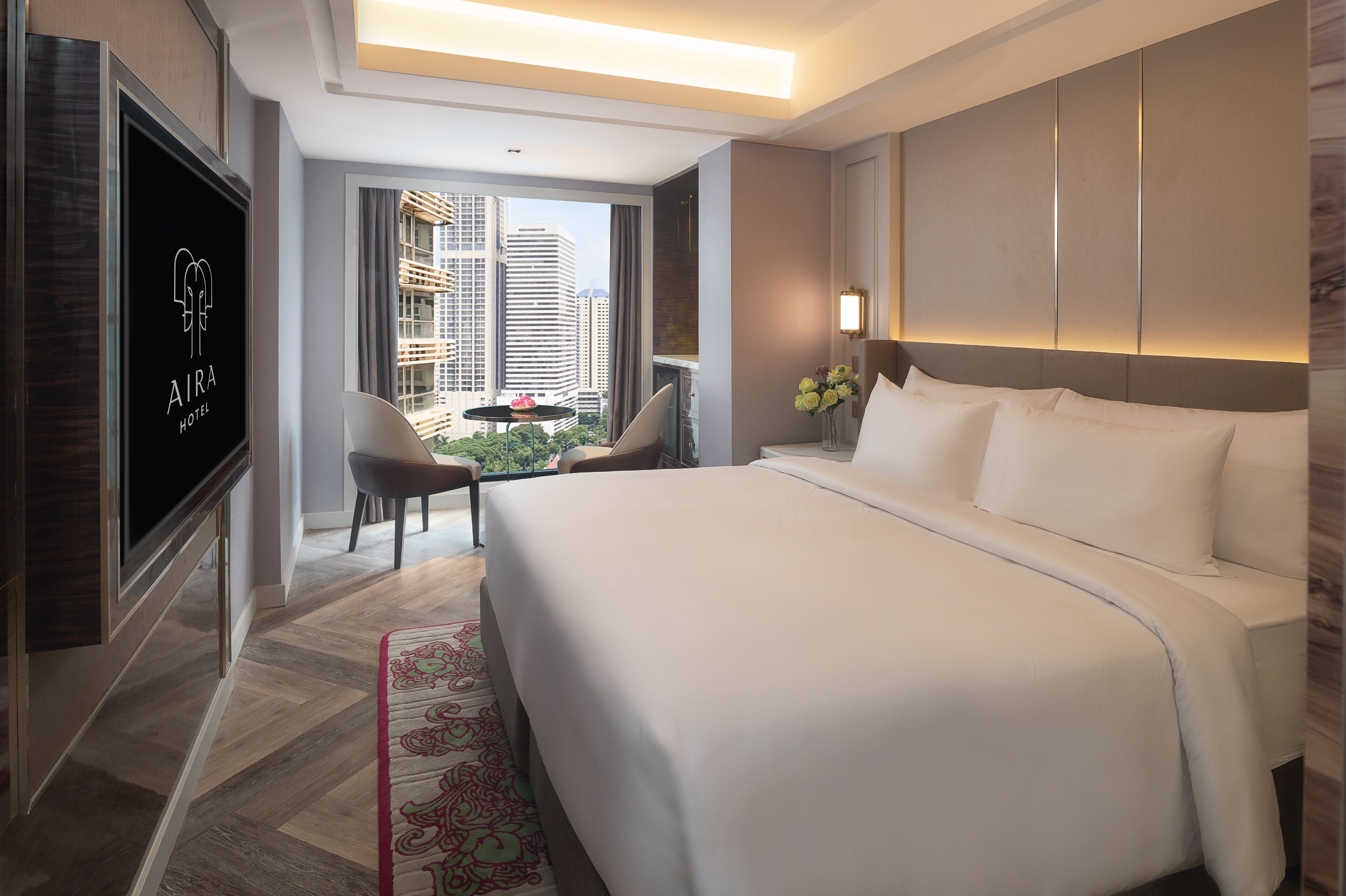 A modern hotel room with a large bed, a TV, a balcony with a view of the city, and a small seating area.