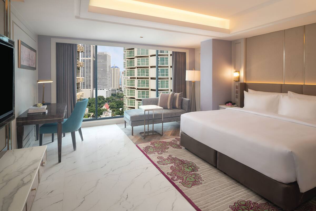 Habitación de hotel con una cama grande, un escritorio con silla, televisor y vista a edificios altos.
