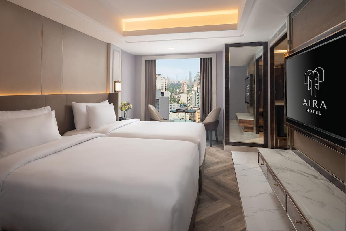 Habitación de hotel con dos camas, televisión, escritorio con silla y vista a la ciudad.