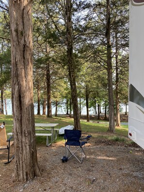 Relax in a serene natural setting with a picnic table and comfortable seating, surrounded by a tranquil body of water and forest.