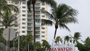 A sign for Sea Watch Restaurant with a view of a tall building and palm trees in the background.