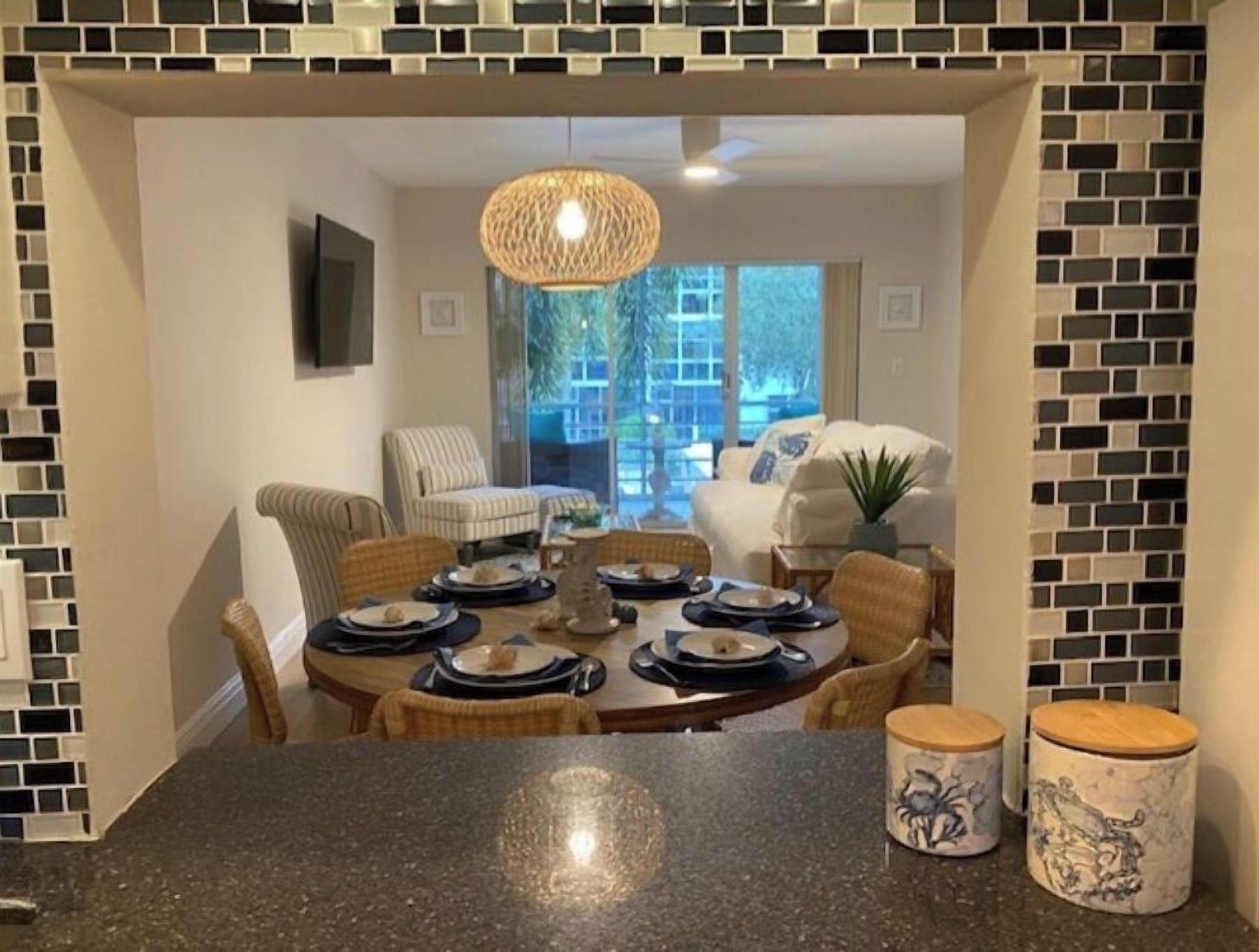 A dining area with a round table set for four, surrounded by wicker chairs. There is a hanging light fixture above the table.