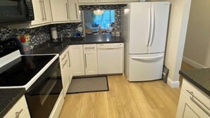 A kitchen with white cabinets, a black countertop, a microwave, a refrigerator, and a small potted plant on top.