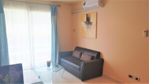 A living room with a sofa, a glass coffee table, and a painting on the wall. - Park Lane Resort Jomtien With Large Lagoon Swimming Pool (Pattaya)