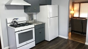 Una cocina compacta con estufa, horno y refrigerador, armarios grises y piso de madera.