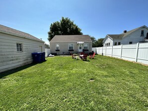 A backyard with a lawn, a barbecue grill, and a dining area with outdoor furniture.