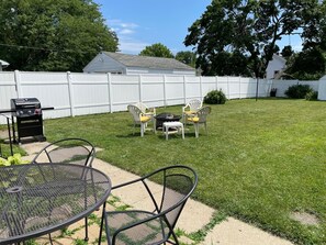 A backyard with a grill, a round metal table, and two chairs.