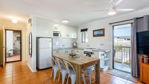 A modern kitchen with white cabinets, a wooden dining table, and a ceiling fan. - Driftwood on the Beach - Sea View Unit 10 (Yeppoon)