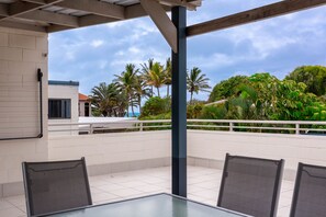 An outdoor patio with a table and chairs, a white brick wall, and a view of palm trees and a building in the background.