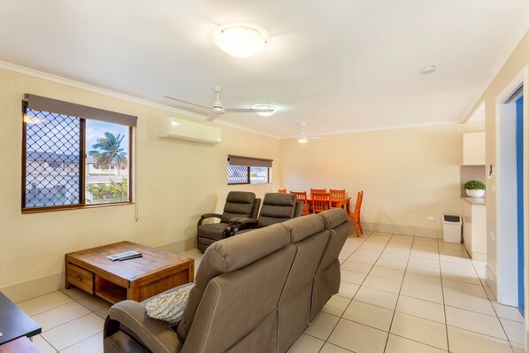 A living room with a sofa, chairs, a table, and a ceiling fan.
