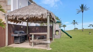 Een achtertuin met een barbecueplek, een houten bank en een speeltoestel.