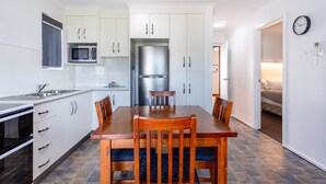 A modern kitchen with white cabinets, a stainless steel refrigerator, and a dining table with chairs.