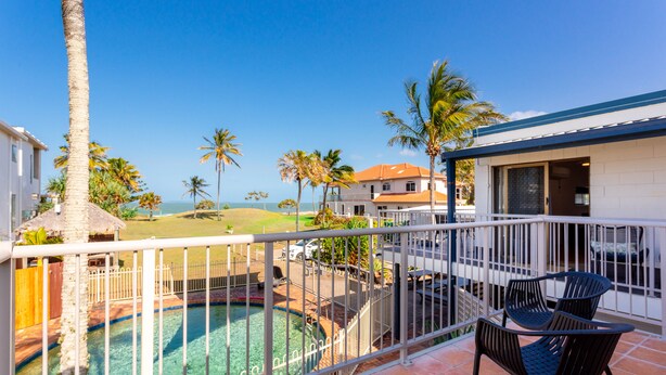 A balcony with a view of a swimming pool, palm trees, and a beach.