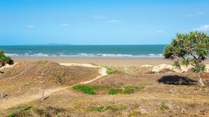 A beach with a clear sky, sandy dunes, and sparse vegetation.