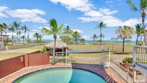 A swimming pool with a thatched-roof hut, palm trees, and a view of the ocean.