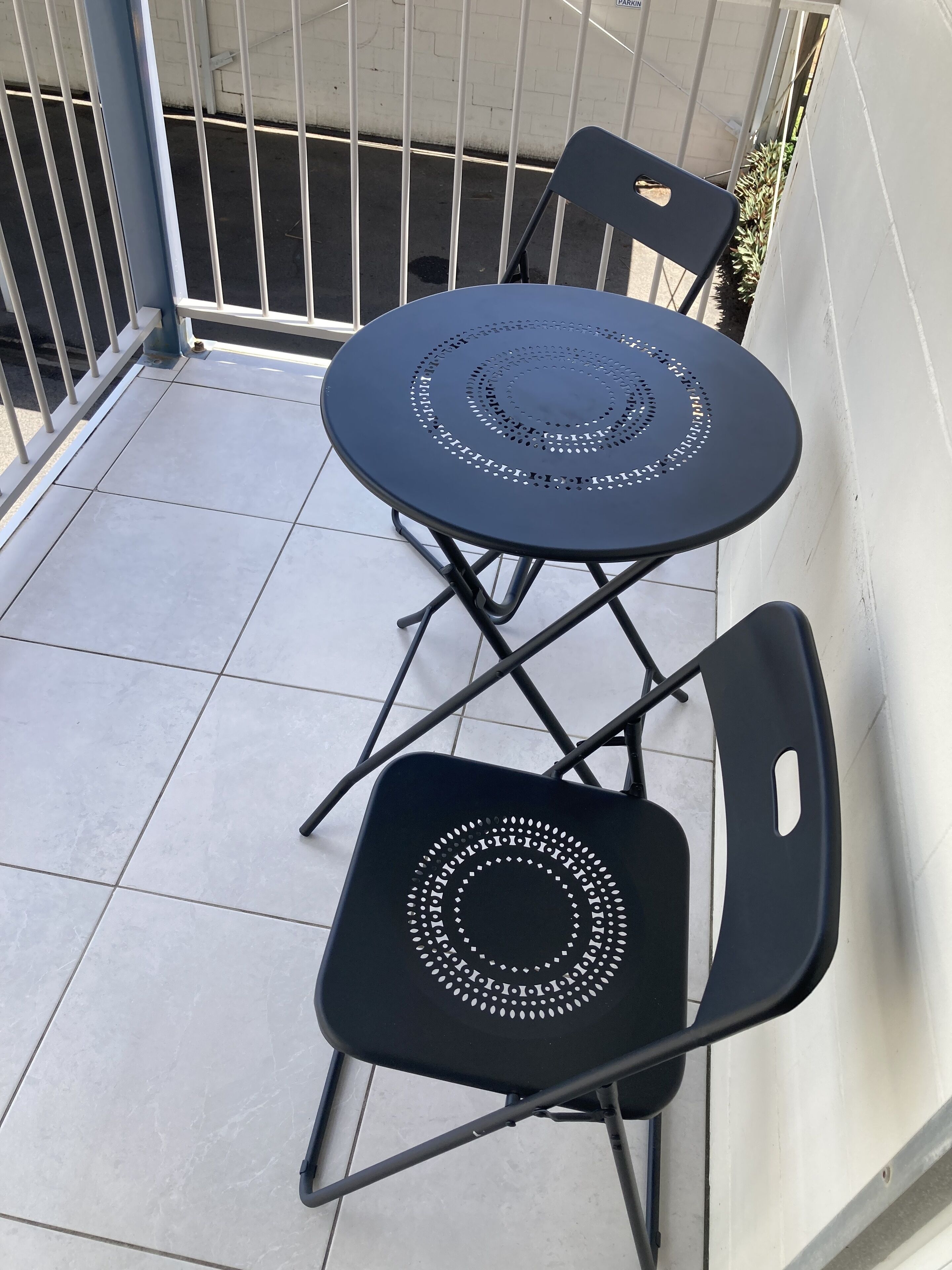 Een klein balkon buiten met een ronde tafel en twee stoelen.