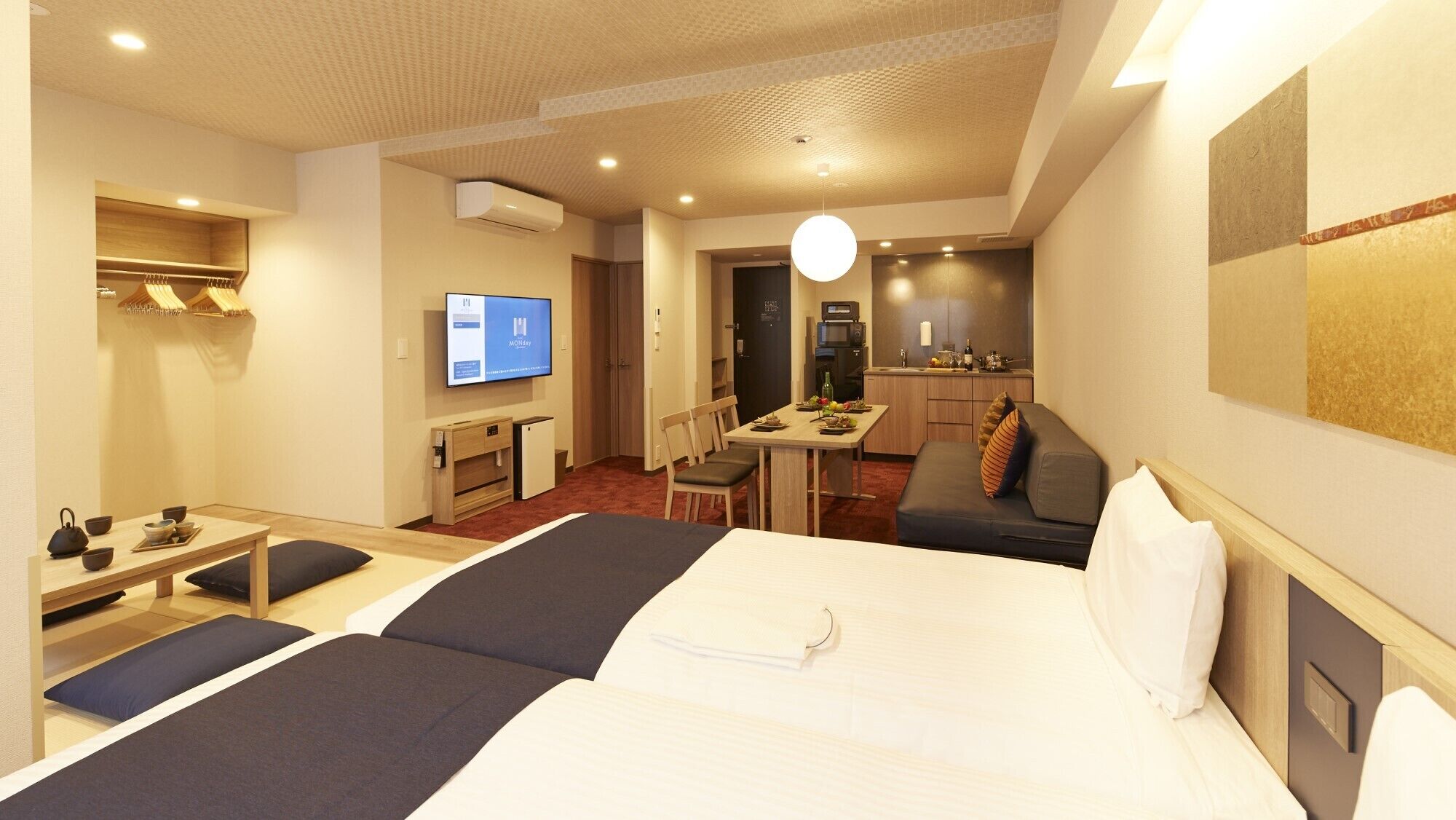 Una habitación de hotel con cama, escritorio, mesa de comedor, televisor y kitchenette.