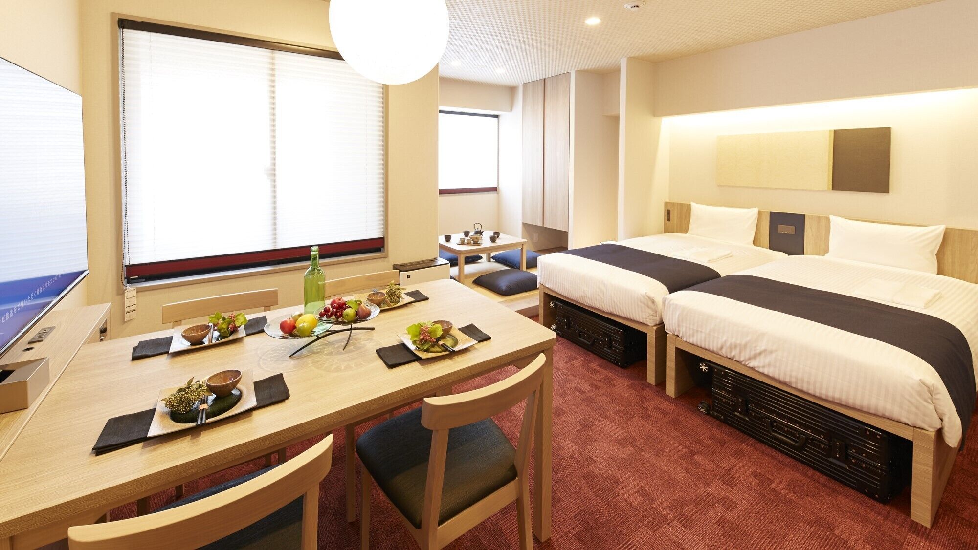 Habitación de hotel con escritorio, dos camas, zona de comedor y un ventanal grande.