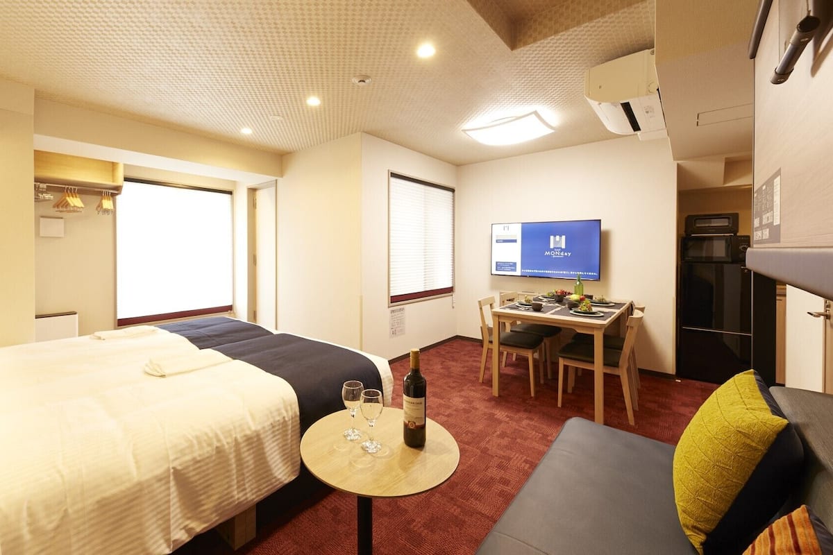 Hotellihuone, jossa on sänky, pieni ruokapöytä tuoleineen, televisio ja pieni keittiönurkkaus.