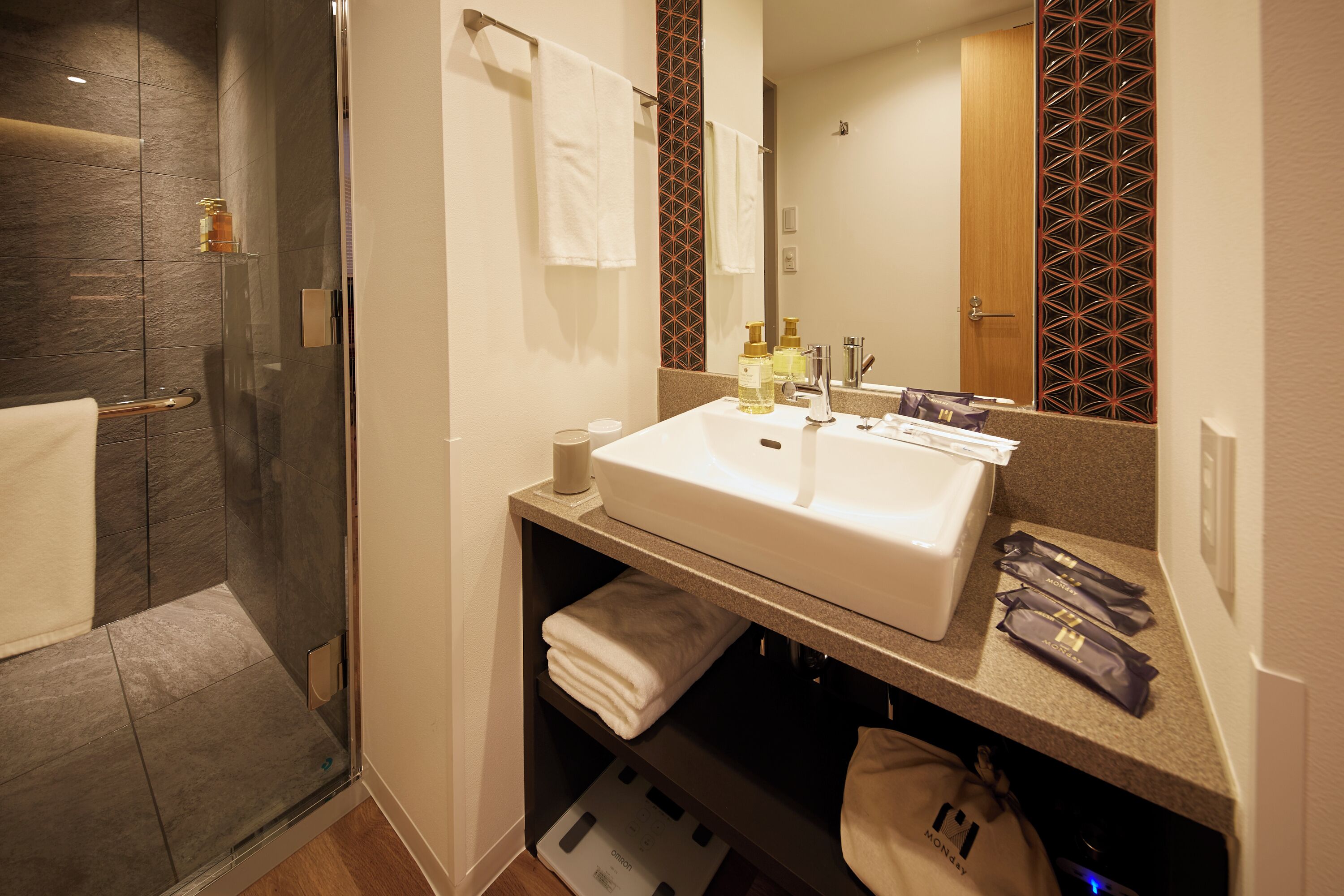 Une salle de bain avec une douche à parois de verre, un lavabo blanc avec un miroir au-dessus, et un porte-serviettes avec des serviettes blanches.