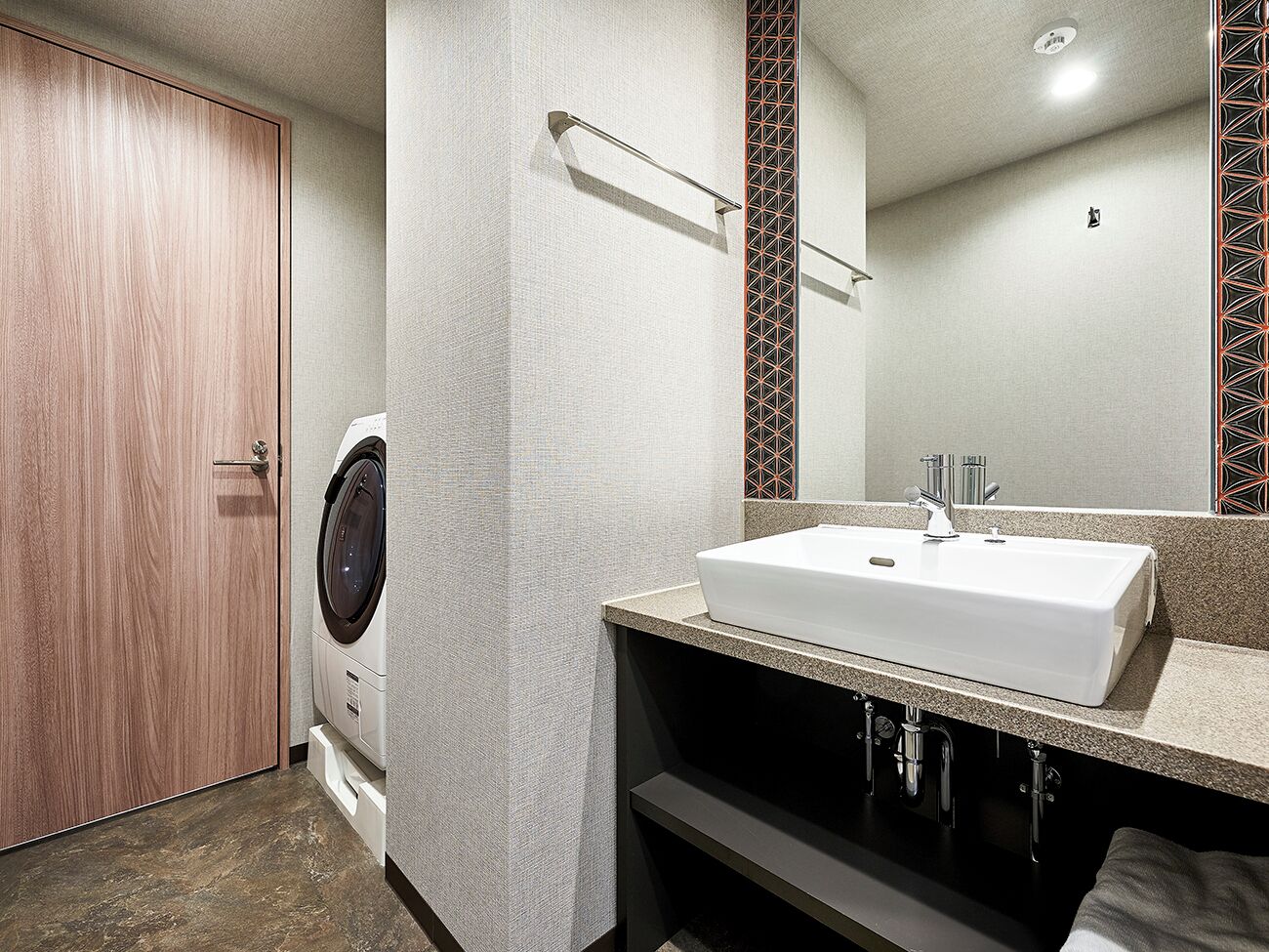 Ein modernes Badezimmer mit integrierter Waschmaschine und Trockner, einem großen Spiegel und einem Waschbecken mit Granitplatte.
