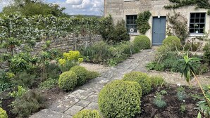 A stone house with a blue door, surrounded by a well-maintained garden with various plants and a stone pathway.