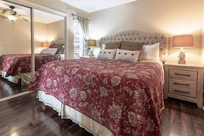 A bedroom with a large bed, a nightstand, a lamp, and a ceiling fan.