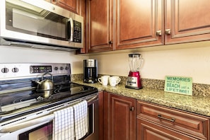 A kitchen with a stove, microwave, coffee maker, and a blender on the counter.