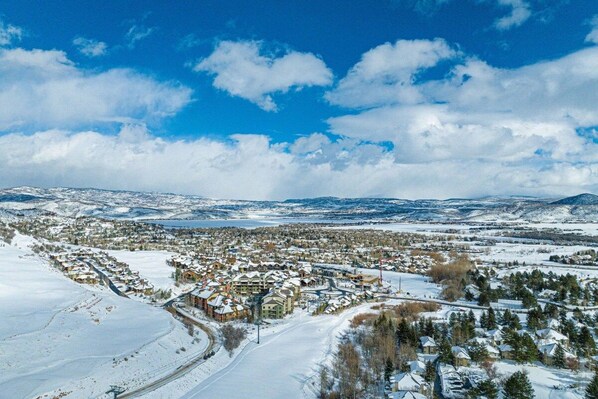 A snow-covered town with a mix of residential and commercial buildings, a clear sky, and distant mountains.