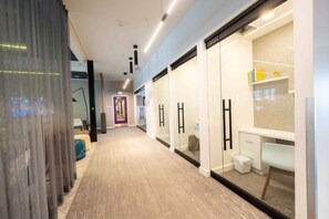 A hallway with a carpeted floor, glass doors, a desk with a chair, and a small trash bin.