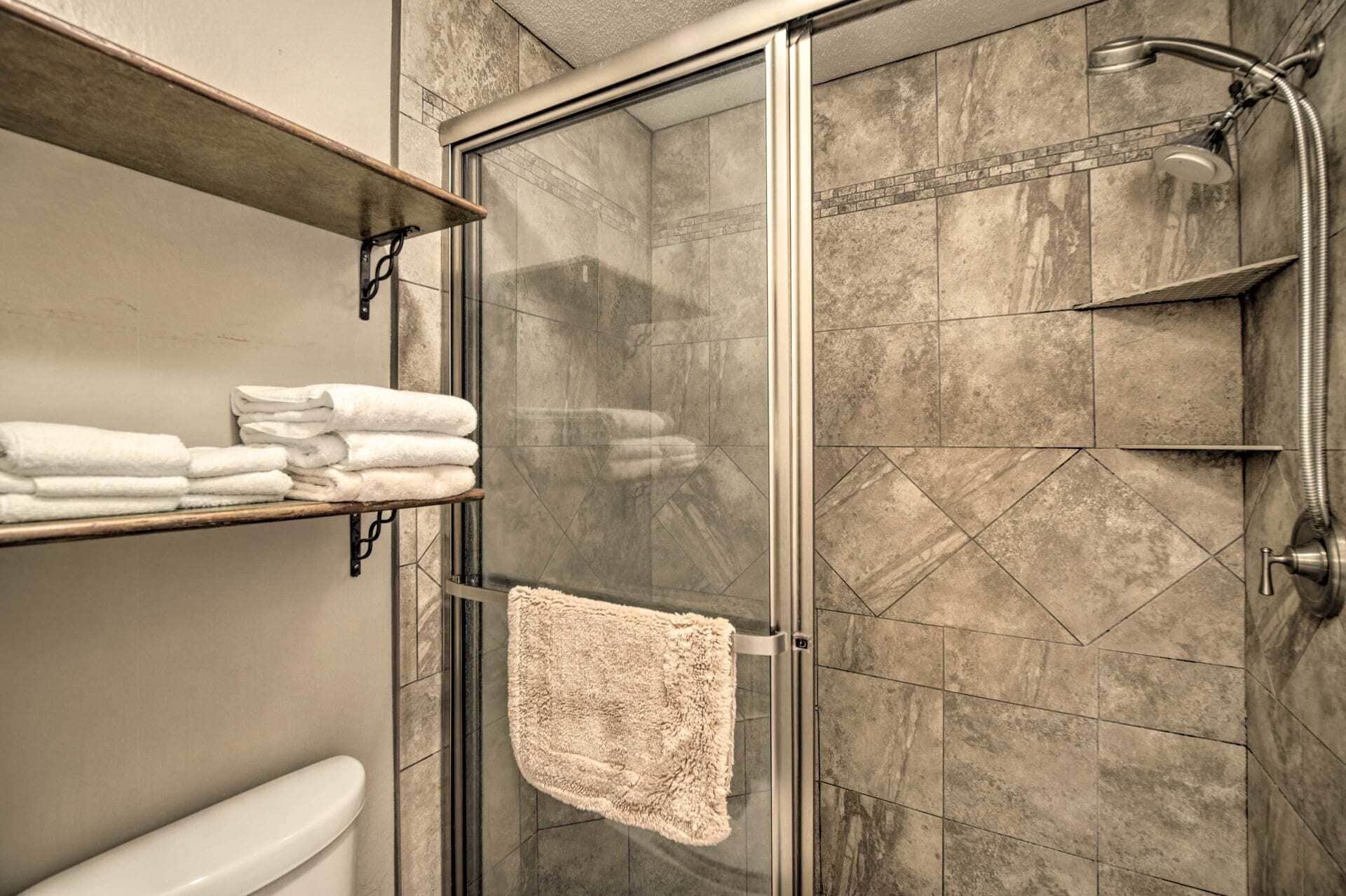 A shower area with a glass door, a towel rack with folded towels, and a showerhead.