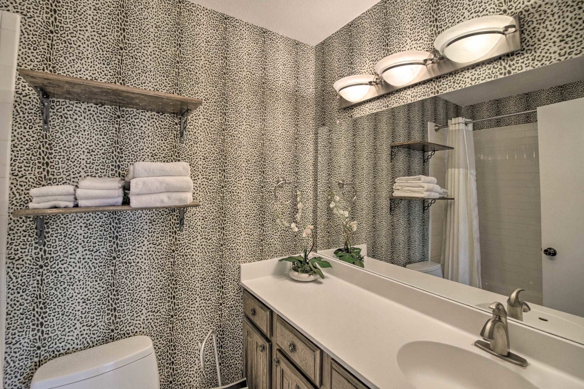 A bathroom with leopard print wallpaper, a sink with a mirror, and shelves with towels.