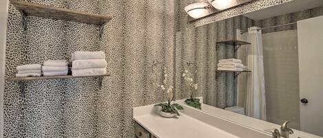 A bathroom with leopard print wallpaper, a sink with a mirror, and shelves with towels.