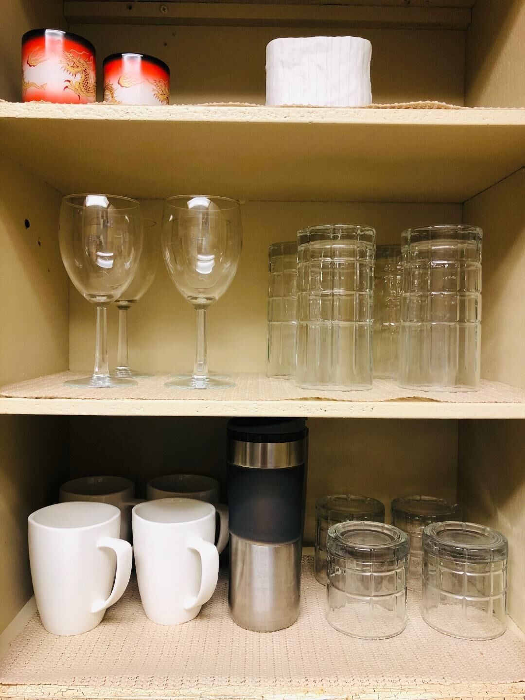 A shelf with two wine glasses, several clear glass mugs, and a stainless steel thermos.