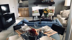 A dining area with a glass table set for four, surrounded by blue sofas and a kitchen in the background. - Houston Med Center/NRG Area 2B/2B All Inclusive (Houston)