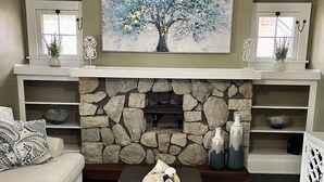 Uma sala de estar com lareira de pedra, um sofá, uma mesa de centro e um quadro sobre a lareira.