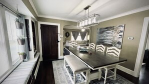 Uma sala de jantar com uma mesa comprida, bancos e um candelabro. Há também um sofá e um quadro na parede.