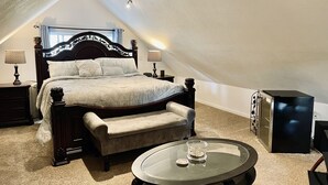 Quarto com uma cama grande, um sofá pequeno, uma mesa de centro de vidro e uma televisão.