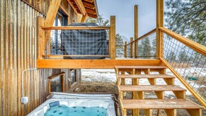 Eine Holzhütte mit Whirlpool, überdachter Außenbereich und einer Treppe zu einer Terrasse.