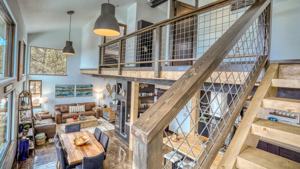 Ein geräumiger Wohnbereich im Loft-Stil mit einer hohen Holztreppe, einem Esstisch und einer gemütlichen Sitzecke.