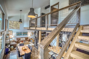 A spacious loft-style living area with a high wooden staircase, a dining table, and a cozy seating area.