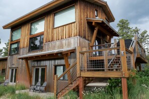 Eine zweistöckige Holzhütte mit großen Fenstern, einer Terrasse und einer Treppe.