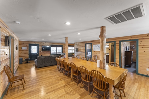 A spacious dining area with a long wooden table and chairs, a sofa, and a television.