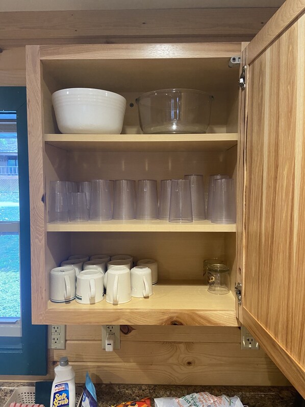 A kitchen with wooden cabinets, a countertop, and various kitchenware including cups, mugs, and a coffee maker.