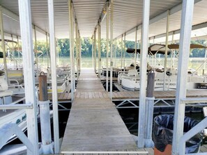 A covered dock with boats moored on either side, a wooden walkway, and a view of a lake. - Lake Cabin (Forsyth)