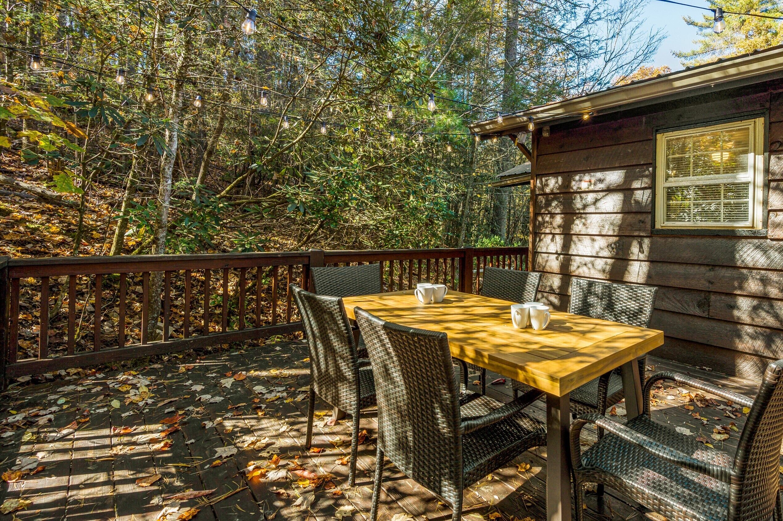 Een houten terras met een tafel en stoelen, omringd door bomen en een houten chalet.